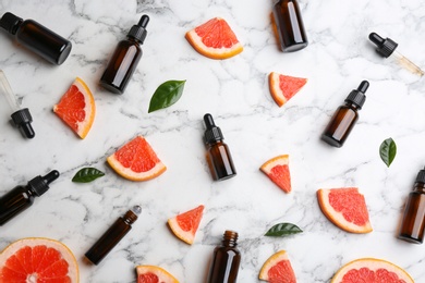 Photo of Flat lay composition with grapefruit slices and bottles of essential oil on marble background