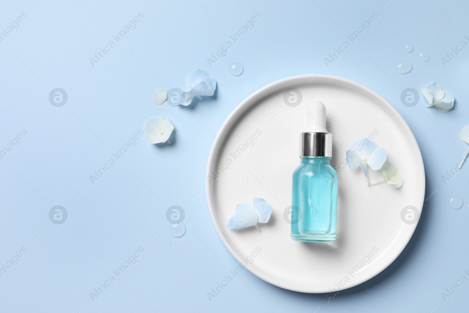 Photo of Bottle of cosmetic serum and beautiful flowers on light blue background, flat lay. Space for text