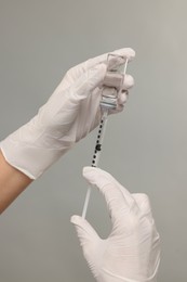 Photo of Doctor filling syringe with medication from glass vial on grey background, closeup