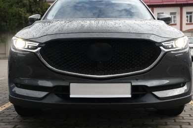 Photo of Black car with switched on headlights in drops of water parked outdoors
