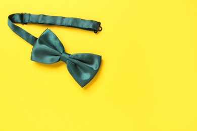 Photo of Stylish green satin bow tie on yellow background, top view. Space for text