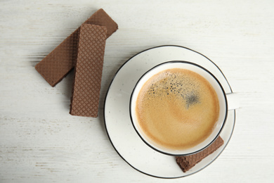 Photo of Delicious wafers and cup of coffee for breakfast on white wooden table, flat lay