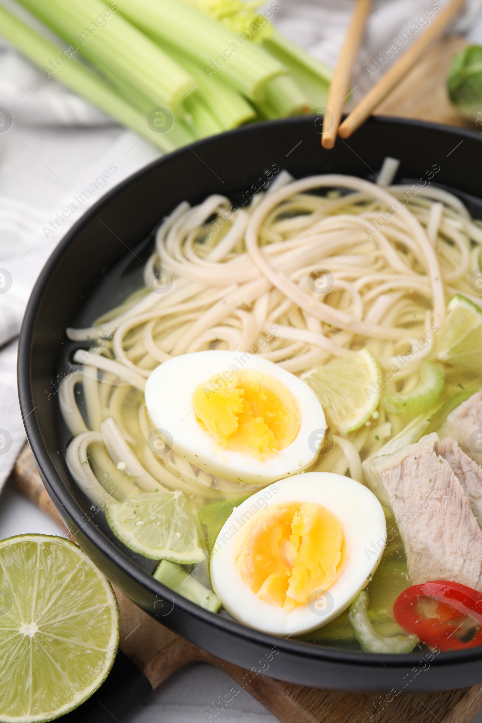 Photo of Bowl of delicious rice noodle soup with meat and egg on white table, closeup