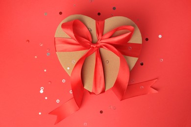 Photo of Beautiful heart shaped gift box with bow and confetti on red background, top view