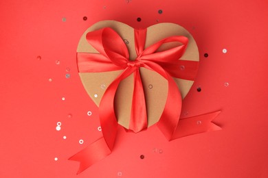 Photo of Beautiful heart shaped gift box with bow and confetti on red background, top view