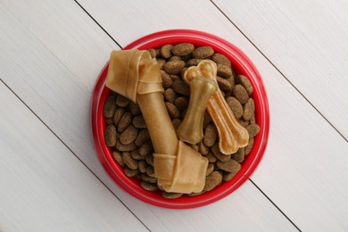 Photo of Dry dog food and treats (chew bones) on white wooden floor, top view