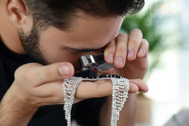 Photo of Male jeweler evaluating beautiful necklace in workshop, closeup