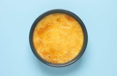 Delicious creme brulee in ceramic ramekin on light blue background, top view