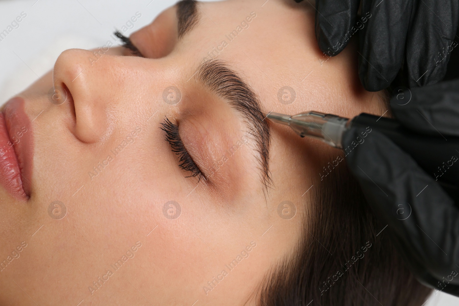 Photo of Beautician making permanent eyebrow makeup to young woman, closeup