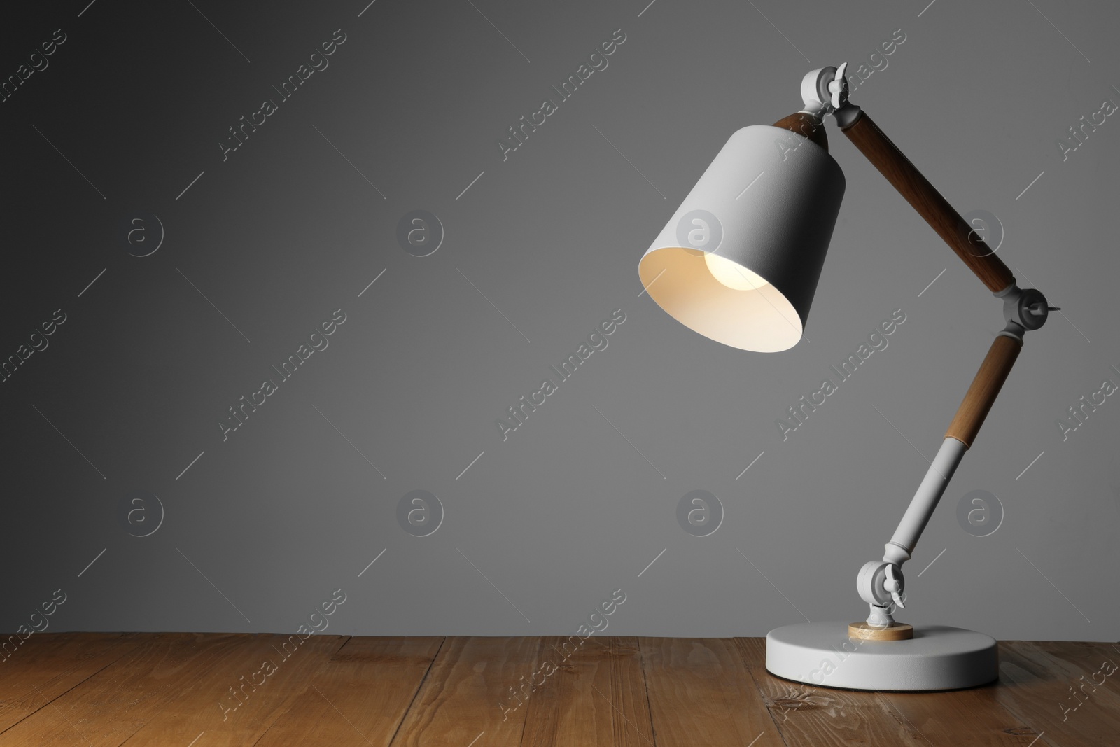 Stylish modern desk lamp on wooden table against grey background, space for text Photo of Stylish modern desk lamp on wooden table against grey background, space for text