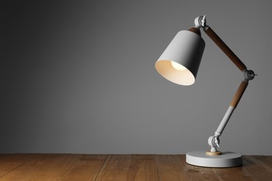 Photo of Stylish modern desk lamp on wooden table against grey background, space for text