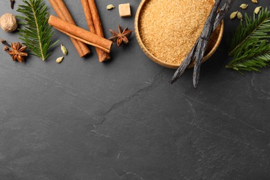 Photo of Different aromatic spices and fir branches on dark textured table, flat lay. Space for text