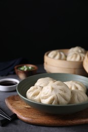 Photo of Delicious bao buns (baozi) in bowl on grey table, closeup