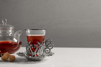 Photo of Glass of traditional Turkish tea in vintage holder, sugar and pot on white table. Space for text