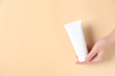 Photo of Woman with tube of hand cream on beige background, closeup. Space for text