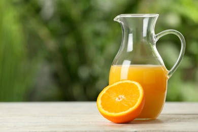 Photo of Tasty orange juice in glass jug on white wooden table against blurred background. Space for text