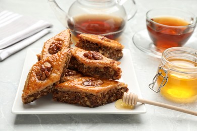 Photo of Delicious baklava with walnuts and honey on light grey marble table