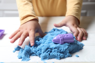 Photo of Little child playing with light blue kinetic sand at white wooden table, closeup