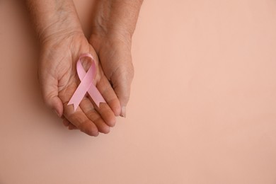 Photo of Senior woman holding pink ribbon on beige background, top view with space for text. Breast cancer awareness