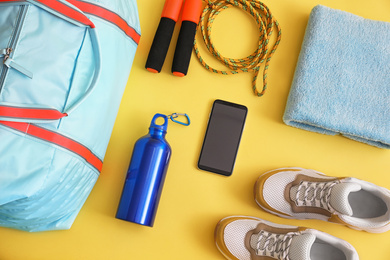 Photo of Gym bag, smartphone and sports equipment on yellow background, flat lay