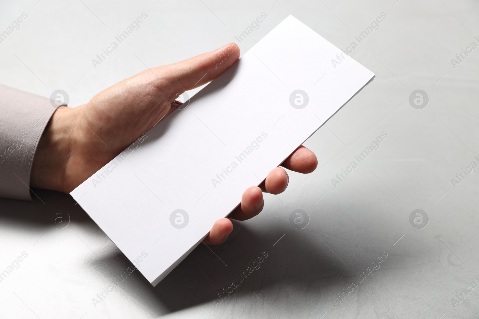 Photo of Man holding white blank card at light grey table, closeup. Mockup for design