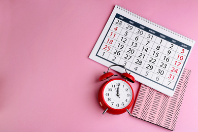 Photo of Calendar, notebook and alarm clock on pink background, flat lay. Space for text