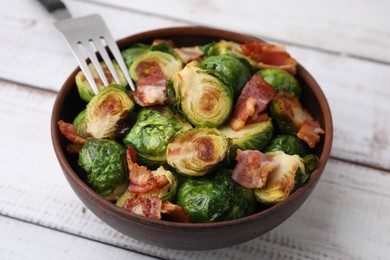 Photo of Delicious roasted Brussels sprouts and bacon in bowl on light wooden table, closeup
