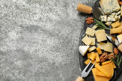 Photo of Cheese platter with specialized knives and fork on grey table, top view. Space for text