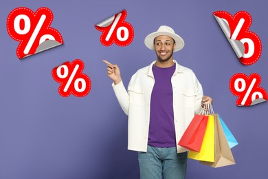 Image of Discount offer. Happy man with paper shopping bags pointing at percent sign stickers on purple background
