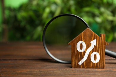 Image of Mortgage rate rising illustrated by percent sign with upward arrow. House model and magnifying glass on wooden table