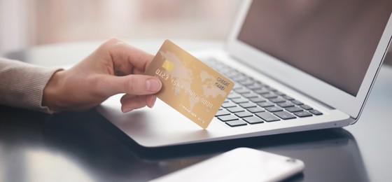 Image of Woman with credit card using laptop for online payment at table, closeup. Banner design