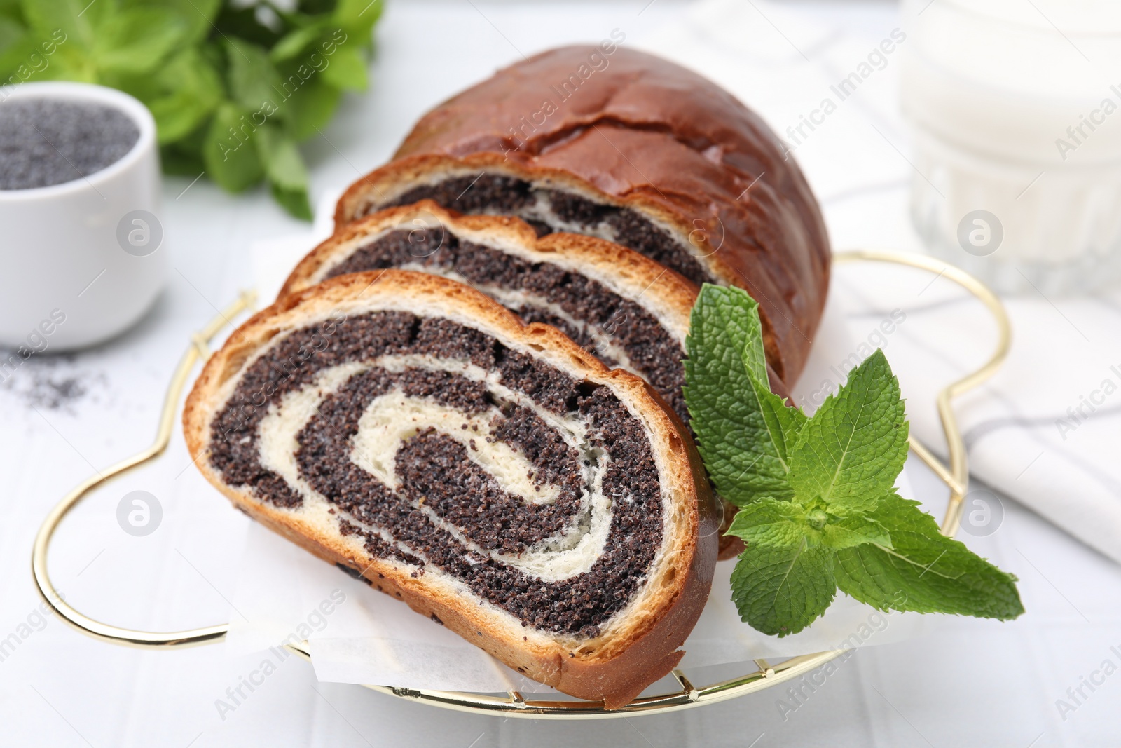 Photo of Slices of poppy seed roll and mint on white table, closeup. Tasty cake