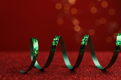 Photo of Shiny green serpentine streamer on red table against blurred lights, closeup