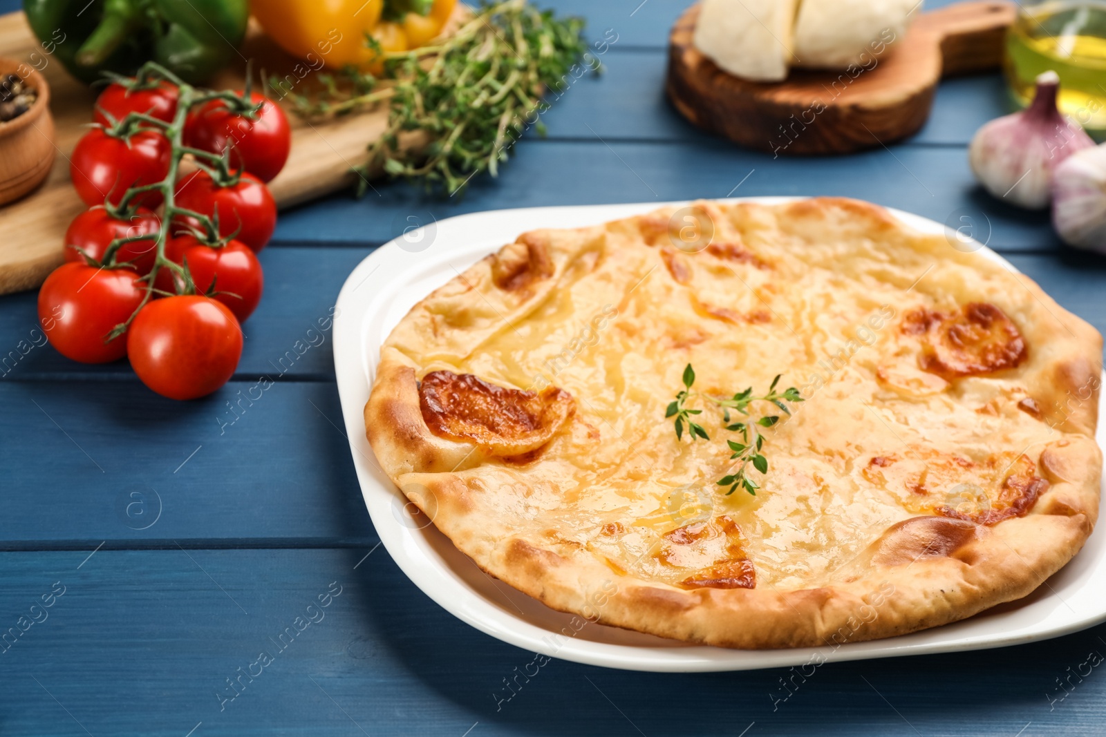 Photo of Delicious khachapuri with cheese, thyme and vegetables on blue wooden table, closeup