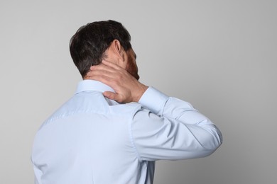 Photo of Man suffering from pain in his neck on light background, back view. Arthritis symptoms