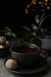 Photo of Cup of aromatic tea and delicious vegan candy ball on grey table against blurred lights, space for text