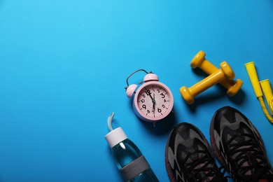 Photo of Sneakers, dumbbells and alarm clock on light blue background, flat lay with space for text. Morning exercise