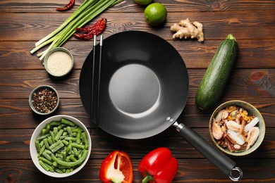 Black wok, chopsticks and products on wooden table, flat lay