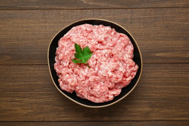 Photo of Bowl of raw fresh minced meat with parsley on wooden table, top view