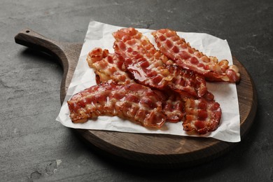 Photo of Board with fried bacon slices on dark textured table, closeup