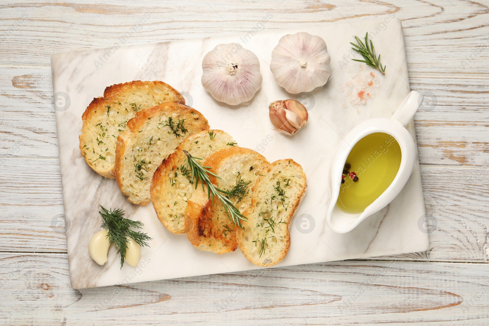 Tasty baguette with garlic, dill, rosemary and oil on white wooden table, top view Photo of Tasty baguette with garlic, dill, rosemary and oil on white wooden table, top view