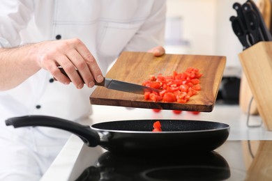 Photo of Chef putting cut tomatoes into frying pan indoors, closeup