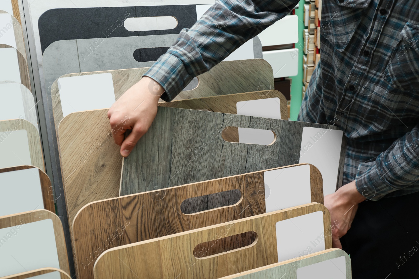 Photo of Man choosing wooden flooring among different samples in shop, closeup