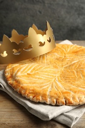 Photo of Traditional galette des Rois with paper crown on wooden table, closeup