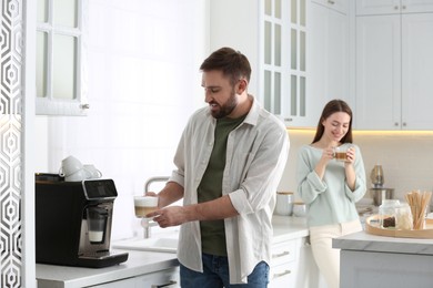 Photo of Young man using modern coffee machine in kitchen