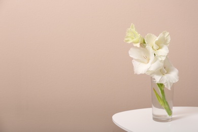 Photo of Vase with beautiful gladiolus flowers on wooden table against beige background. Space for text