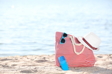 Photo of Bag, sunglasses and hat on sand near sea. Beach object
