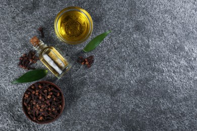 Photo of Essential oil and dried cloves on grey stone table, flat lay. Space for text