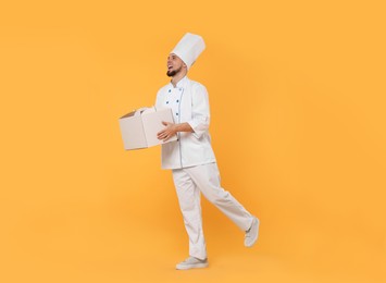 Photo of Happy professional confectioner in uniform holding cake box on yellow background