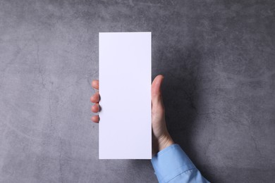 Photo of Woman holding blank card at grey table, top view. Mockup for design